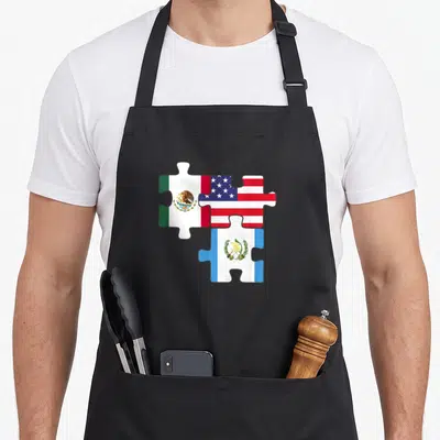 Latinoamerica mexico apron - Three interlocking puzzle pieces showing red, white, blue, and green flags of Mexico, USA — shown on a black cotton canvas apron against a white background