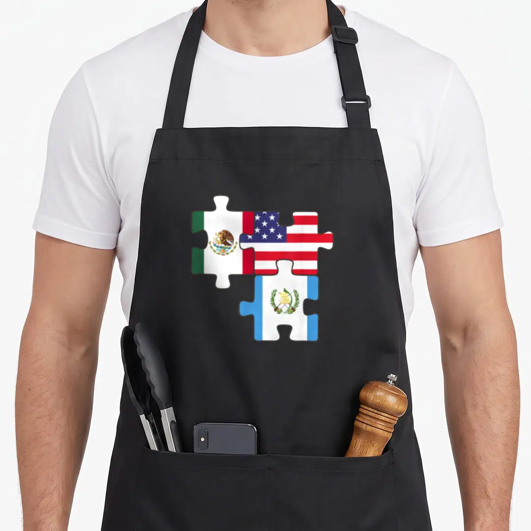 Latinoamerica mexico apron - Three interlocking puzzle pieces showing red, white, blue, and green flags of Mexico, USA — shown on a black cotton canvas apron against a white background