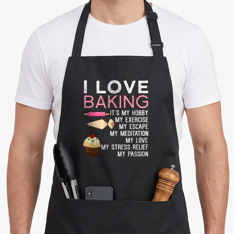 Cake women's christmas aprons - I Love Baking text with pink rolling pin, beige piping bag, and cherry cupcake icons — shown on a black cotton canvas apron against a white background