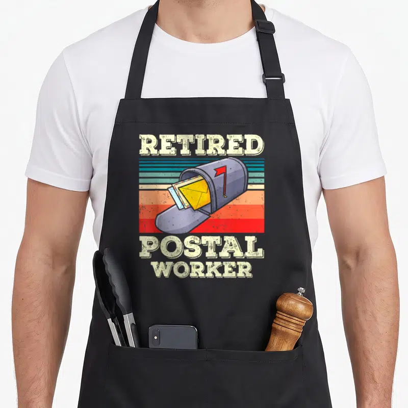 Mail postman postal aprons - retired postal worker text above grey mailbox with yellow envelope and red flag on retro — shown on a black cotton canvas apron against a white background