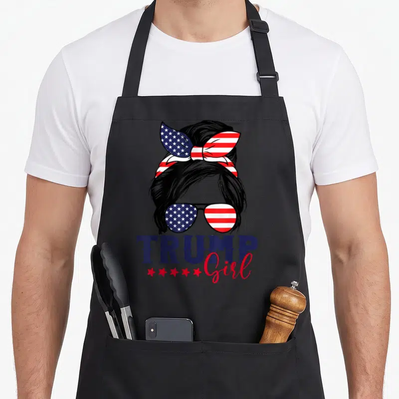 Trump american flag apron - Woman silhouette with US flag bun and sunglasses, TRUMP Girl text in navy and red — shown on a black cotton canvas apron against a white background