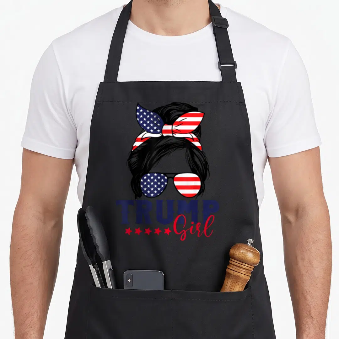 Trump american flag apron - Woman silhouette with US flag bun and sunglasses, TRUMP Girl text in navy and red — shown on a black cotton canvas apron against a white background