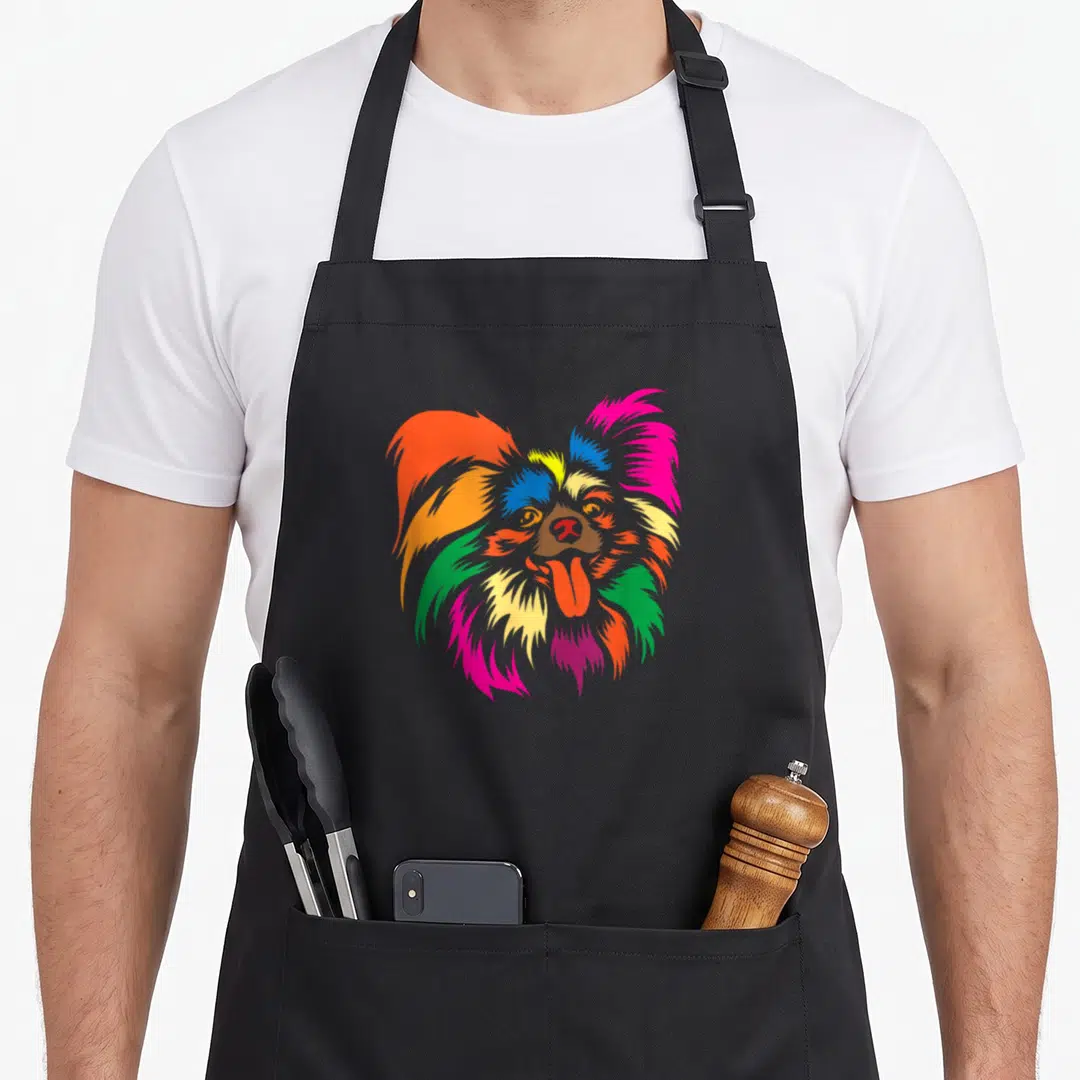 Retro papillon dog apron - Colorful cartoon papillon dog head with orange pink blue yellow green and red fur — shown on a black cotton canvas apron against a white background