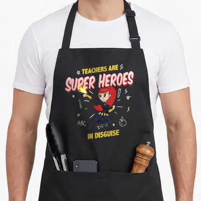 Funny heroe teacher apron - Stacked text TEACHERS ARE SUPER HEROES IN DISGUISE on black apron — shown on a black cotton canvas apron against a white background