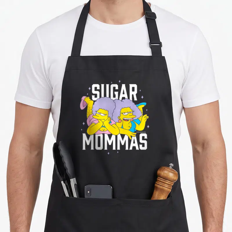 Mommas sugar apron - Two cartoon women with purple hair under SUGAR MOMMAS text — shown on a black cotton canvas apron against a white background