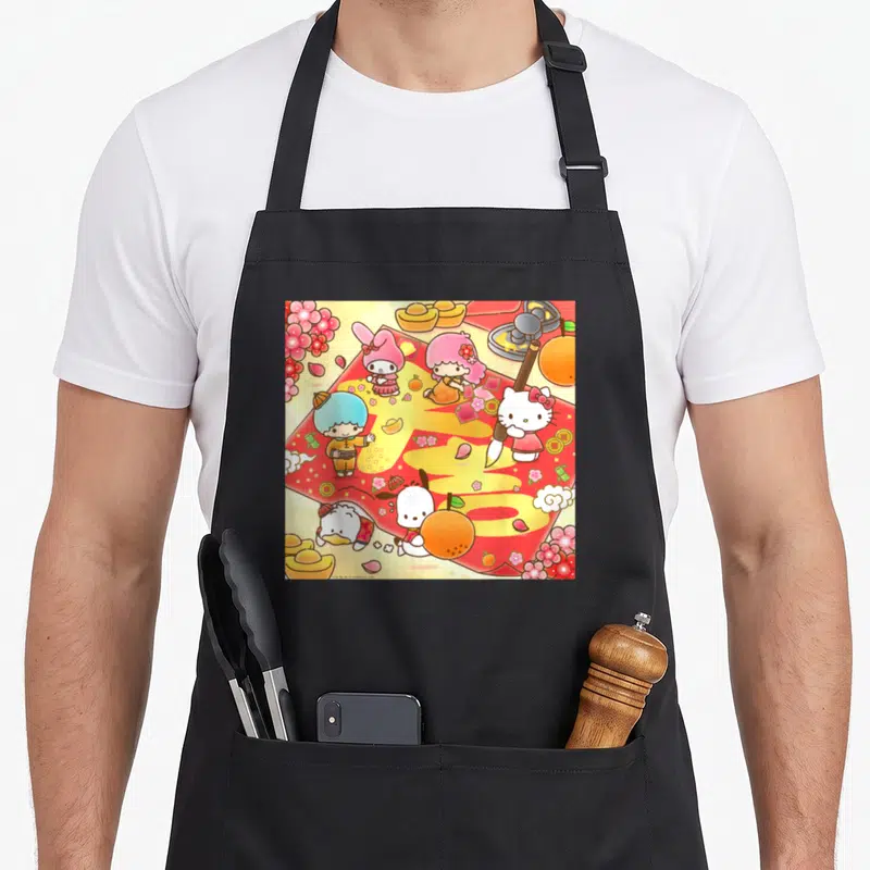 Calligraphy friends apron - Sanrio characters on red sheet with yellow calligraphy, oranges, flowers, and gold ingots — shown on a black cotton canvas apron against a white background