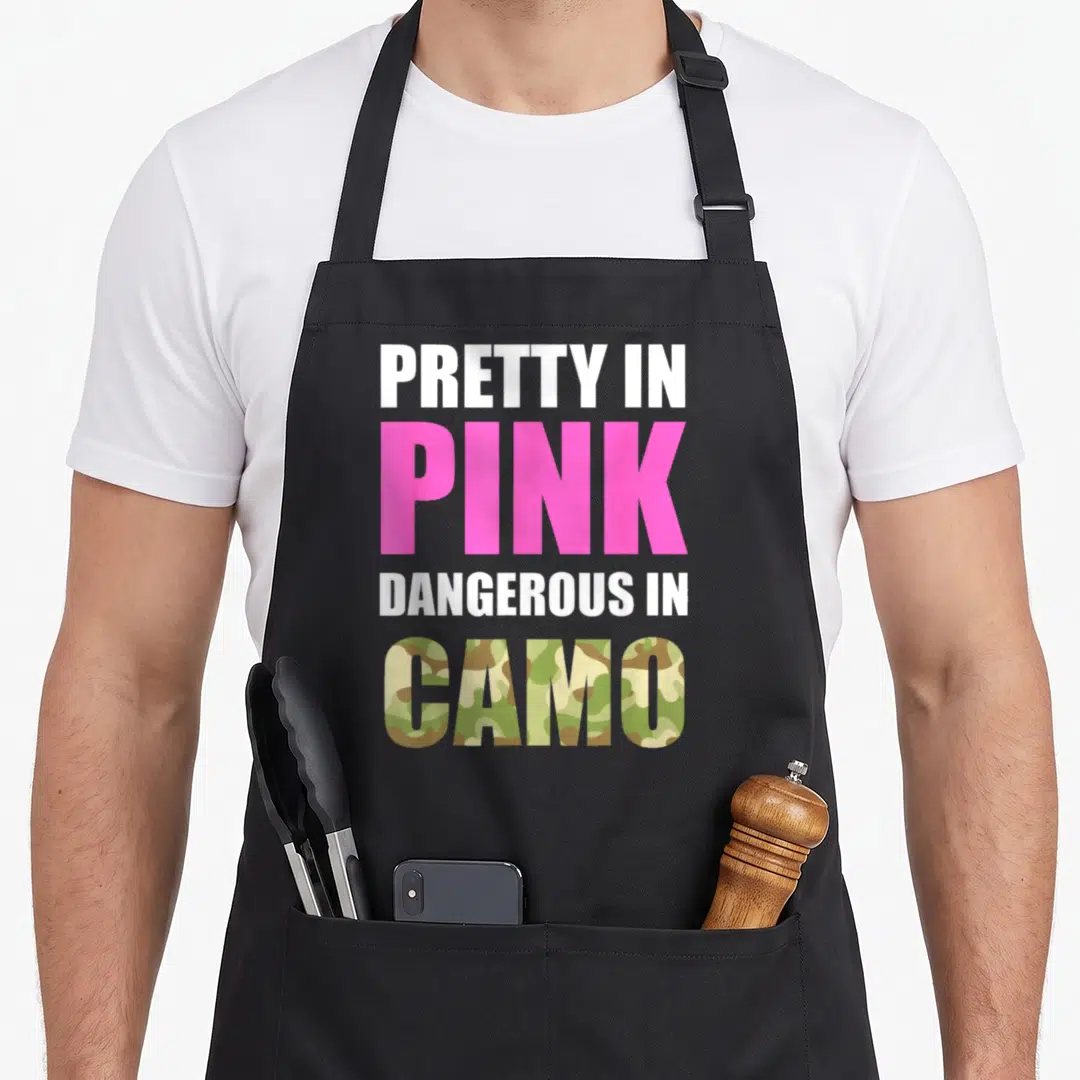 Camoflauge pink camo apron - Stacked text pretty in pink dangerous in camo with pink and camouflage pattern fills — shown on a black cotton canvas apron against a white background