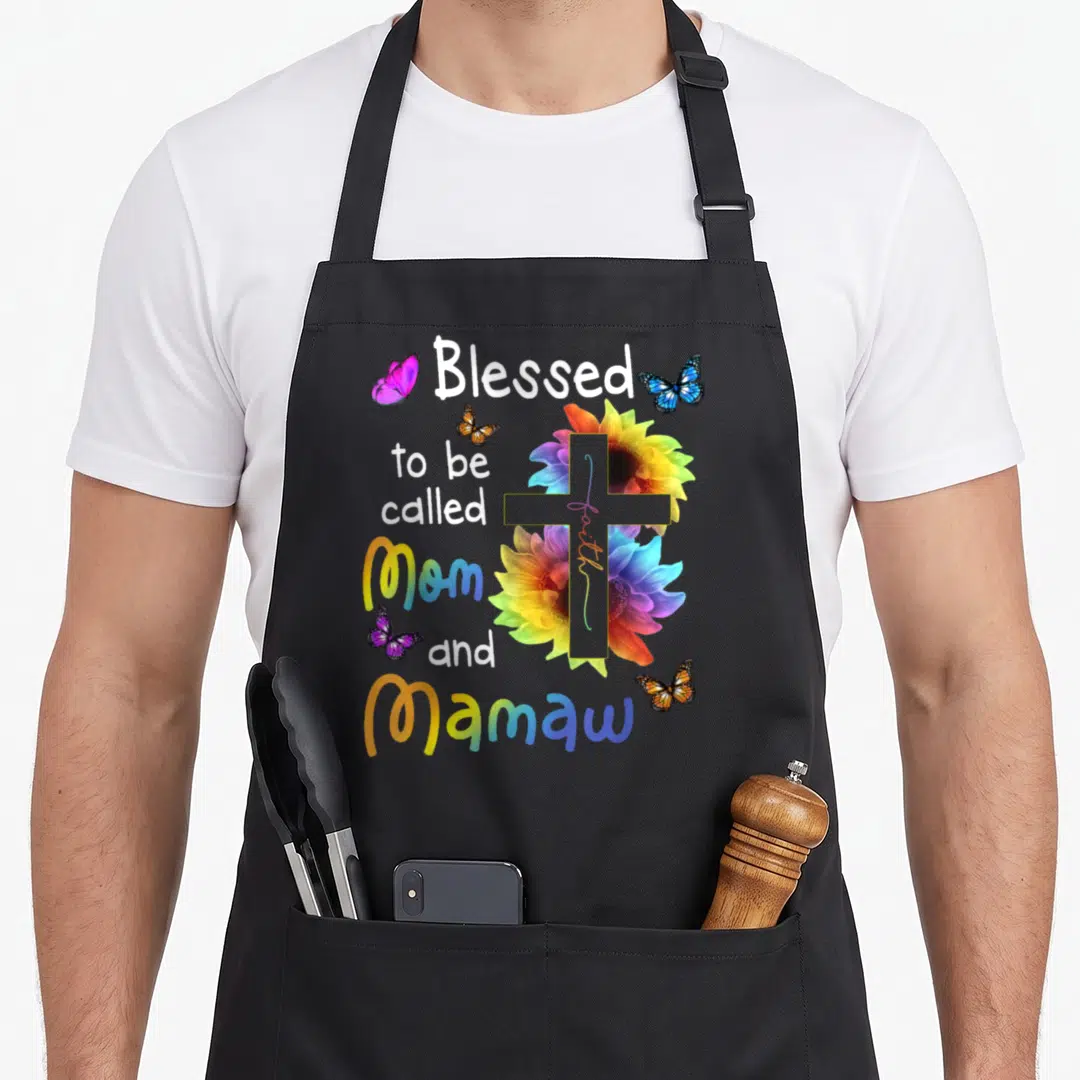 Mamaw christian apron - Blessed to be called Mom and Mamaw text with rainbow sunflowers, cross, and butterflies — shown on a black cotton canvas apron against a white background