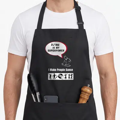 Superpower djing addict apron - Speech bubble reading DJ'ING IS MY SUPERPOWER above DJ silhouette and dancing figures — shown on a black cotton canvas apron against a white background