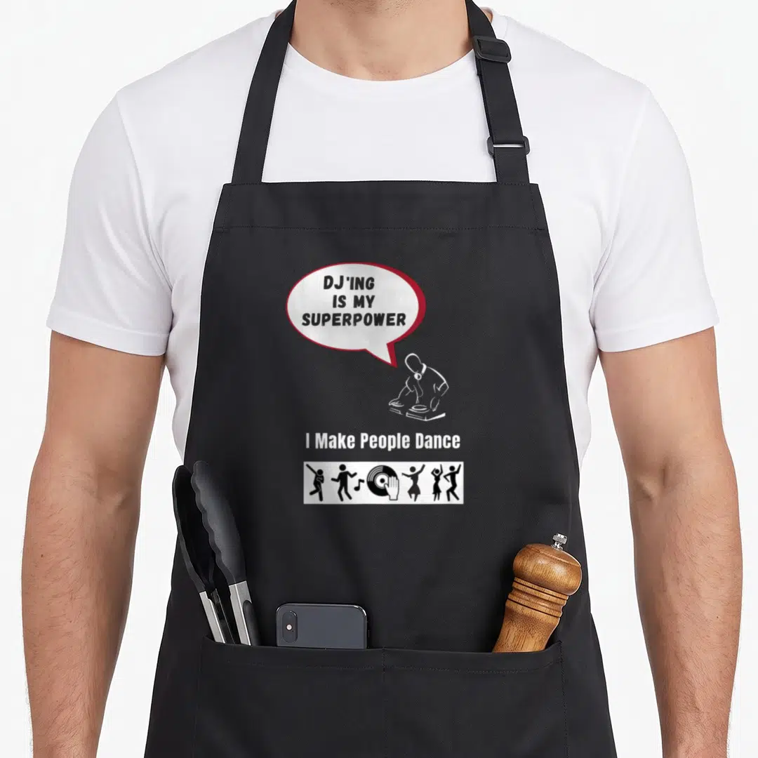 Superpower djing addict apron - Speech bubble reading DJ'ING IS MY SUPERPOWER above DJ silhouette and dancing figures — shown on a black cotton canvas apron against a white background