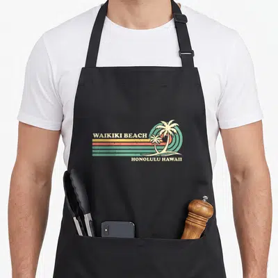 Honolulu summer aprons - Retro Waikiki Beach text with two palm trees and striped sun in teal orange yellow cream — shown on a black cotton canvas apron against a white background