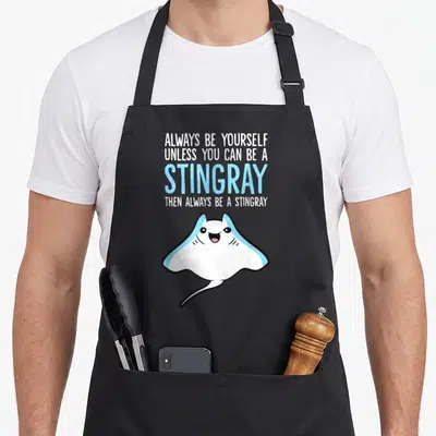 Unless i love my penguin apron - Stacked white and blue text above a smiling cartoon stingray with black outline — shown on a black cotton canvas apron against a white background