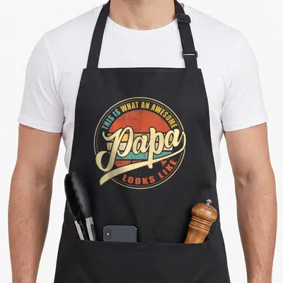 Retro papa grandpa apron - Retro sunset graphic with THIS IS WHAT AN AWESOME Papa LOOKS LIKE text in red orange teal — shown on a black cotton canvas apron against a white background