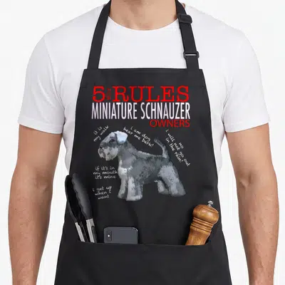 Rule miniature schnauzer apron - Cartoon miniature schnauzer with 5 rules text and handwritten quotes on grey background — shown on a black cotton canvas apron against a white background