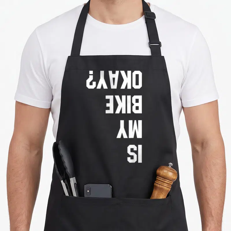 Bmx bike apron - White text IS MY BIKE OKAY rotated 90 degrees on grey background — shown on a black cotton canvas apron against a white background