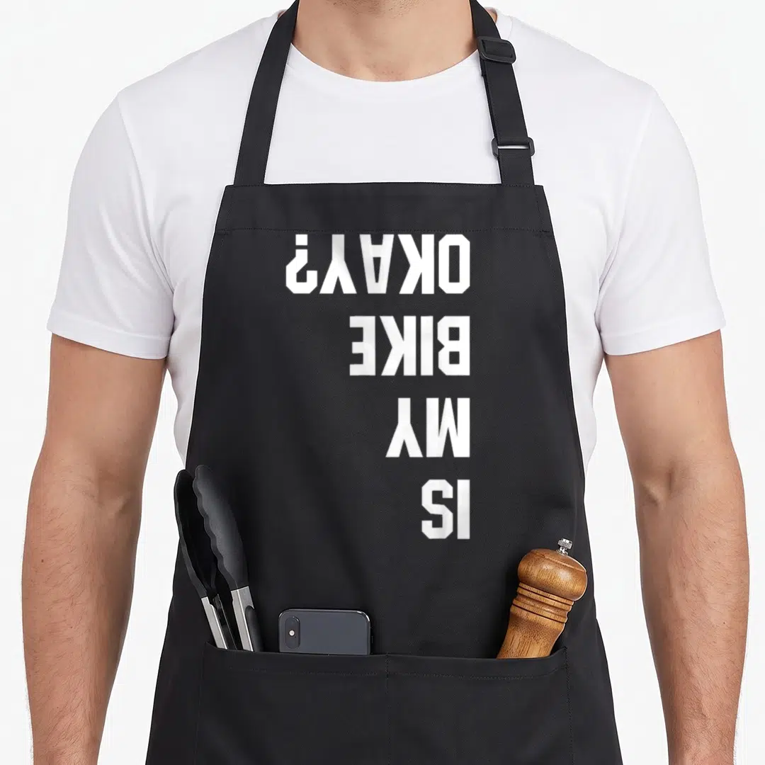 Bmx bike apron - White text IS MY BIKE OKAY rotated 90 degrees on grey background — shown on a black cotton canvas apron against a white background