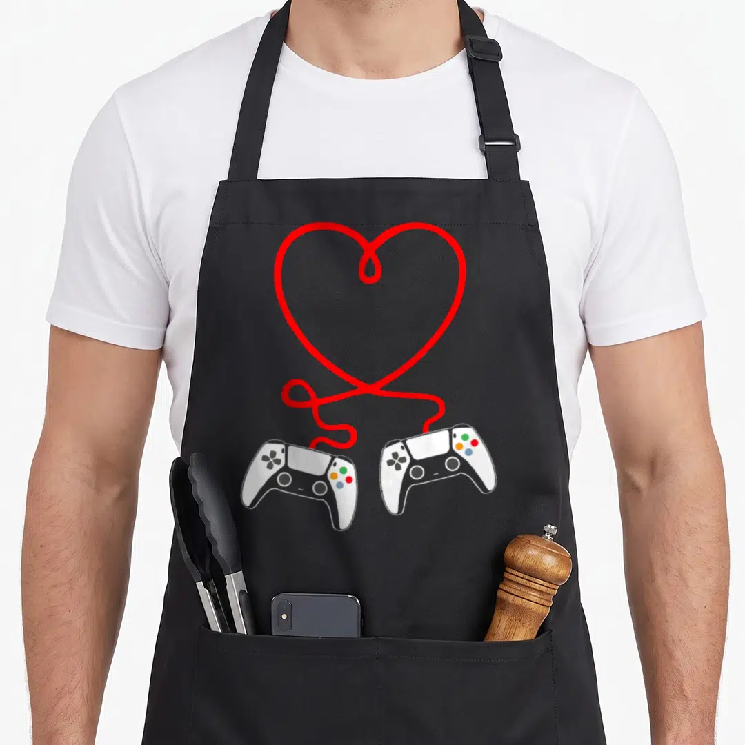 Controller valentine apron - Red heart line connects two white game controllers in cartoon style — shown on a black cotton canvas apron against a white background