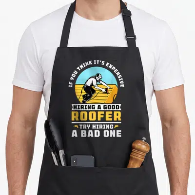 Expensive roofing apron - Cartoon roofer on yellow deck with sarcastic text about hiring good vs bad roofers — shown on a black cotton canvas apron against a white background