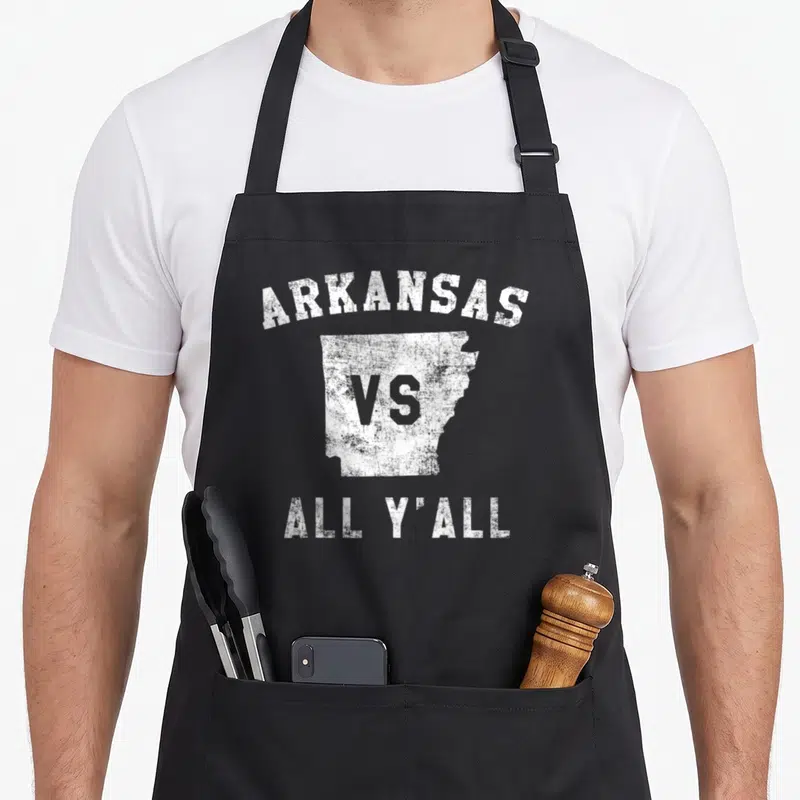 Yall arkansas apron - Distressed white map of Arkansas with arched ARKANSAS VS ALL Y'ALL text — shown on a black cotton canvas apron against a white background