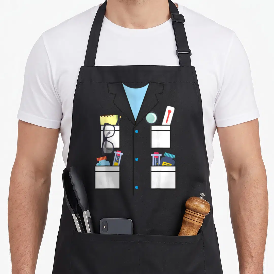 Science halloween apron - Cartoon lab coat with four pockets holding glasses, test tubes, thermometer, and bottles — shown on a black cotton canvas apron against a white background