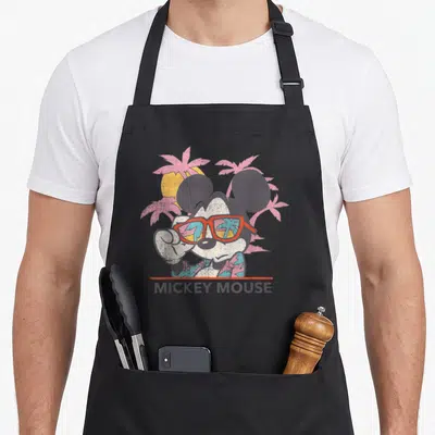 Friend tropical print aprons - Retro Mickey Mouse with sunglasses, pink palms, yellow sun, and red line text — shown on a black cotton canvas apron against a white background