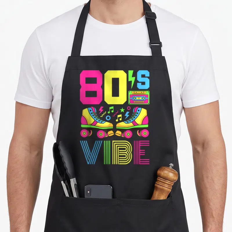 Themed 80s apron - Colorful roller skates cassette tape and 80S VIBE text in pink yellow blue green retro style — shown on a black cotton canvas apron against a white background