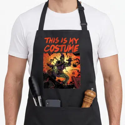 Goblin costume halloween apron - Red text THIS IS MY COSTUME above comic goblin in explosion with orange green purple — shown on a black cotton canvas apron against a white background