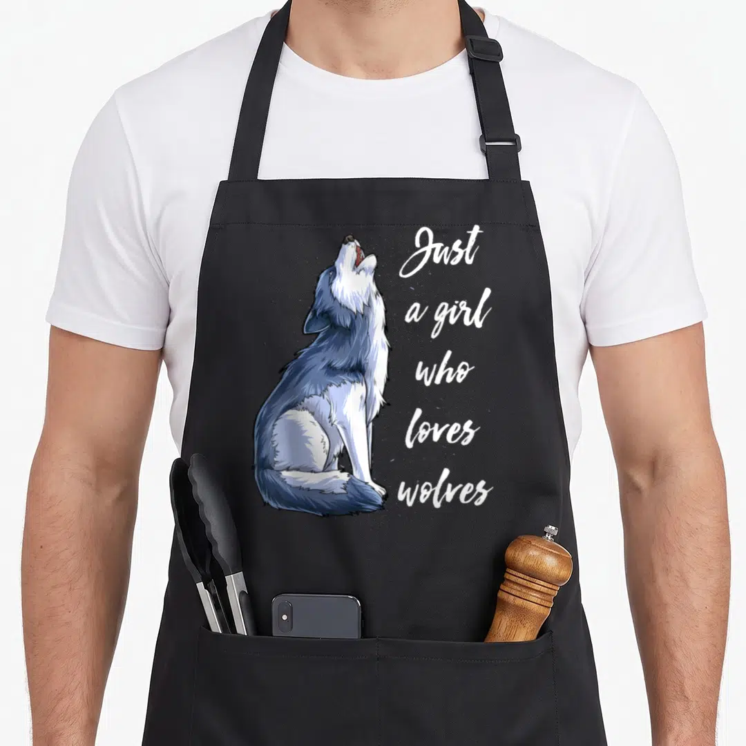 Wolve outdoor apron - Cartoon wolf howling beside stacked white text reading Just a girl who loves wolves — shown on a black cotton canvas apron against a white background