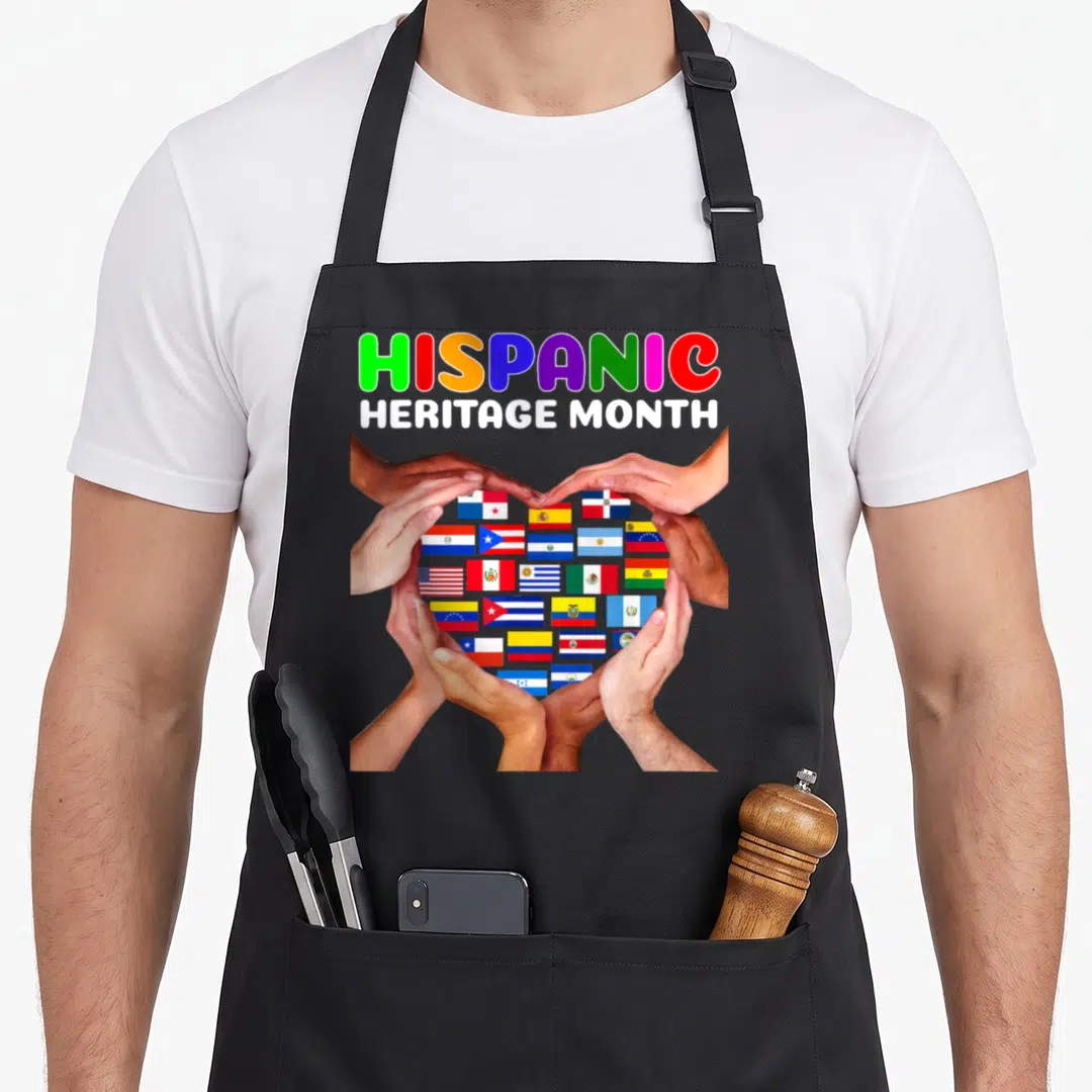 Hispanic country apron - Six hands forming a heart around a grid of national flags under stacked text reading HISPANIC — shown on a black cotton canvas apron against a white background