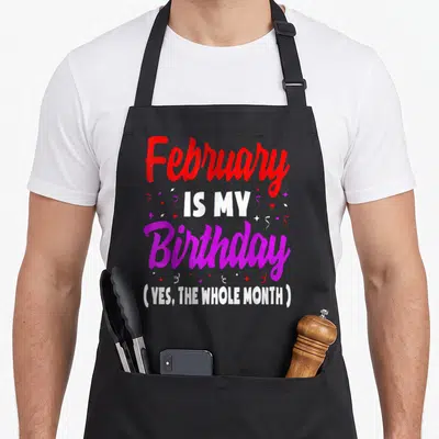 February whole month birthday apron - Red purple and white text reading February is my birthday yes the whole month — shown on a black cotton canvas apron against a white background