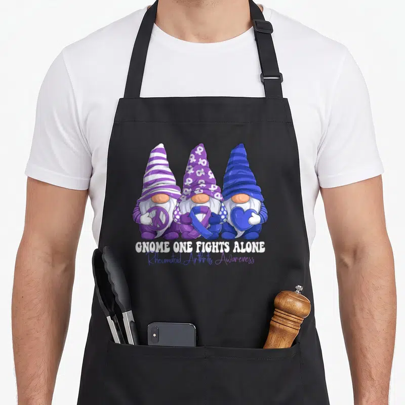 Gnomy rheumatoid ribbon apron - Three gnomes holding peace sign, purple ribbon, and blue heart above awareness text — shown on a black cotton canvas apron against a white background