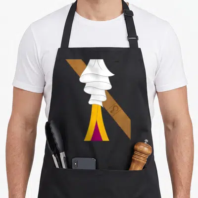 Pan halloween apron - Layered white ruffled fabric over brown diagonal strip and yellow purple cloth — shown on a black cotton canvas apron against a white background