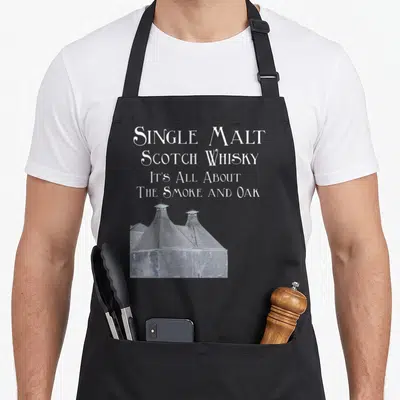 Single malt apron - White text reading Single Malt Scotch Whisky above a distillery silhouette with two chimneys — shown on a black cotton canvas apron against a white background