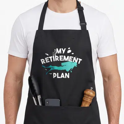 Retirement holiday apron - Teal scuba diver silhouette surrounded by white MY RETIREMENT PLAN text — shown on a black cotton canvas apron against a white background