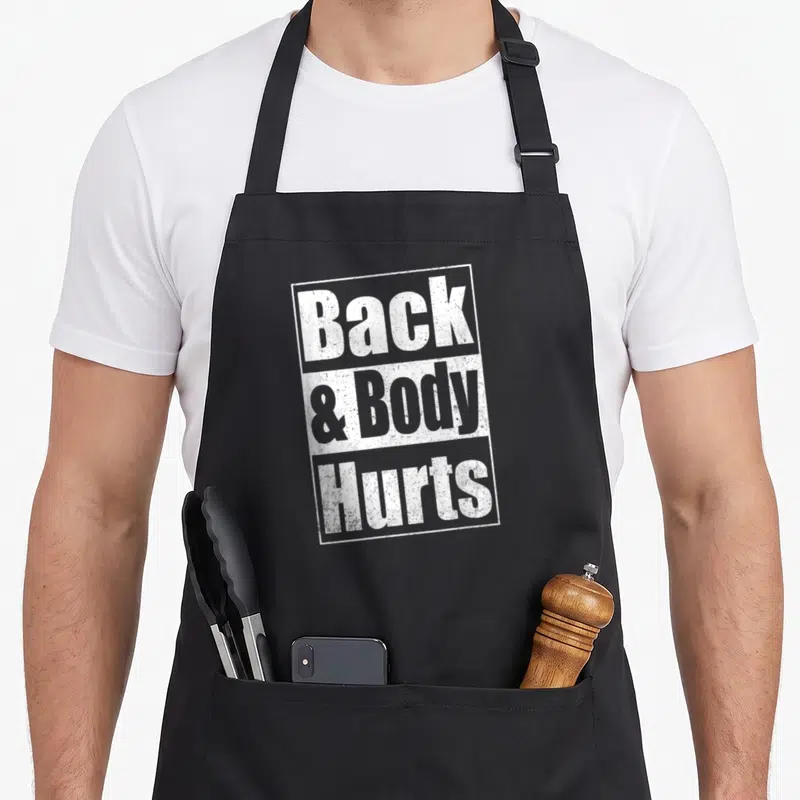 Funny hurt body apron - White stacked text boxes reading Back & Body Hurts in distressed typography — shown on a black cotton canvas apron against a white background