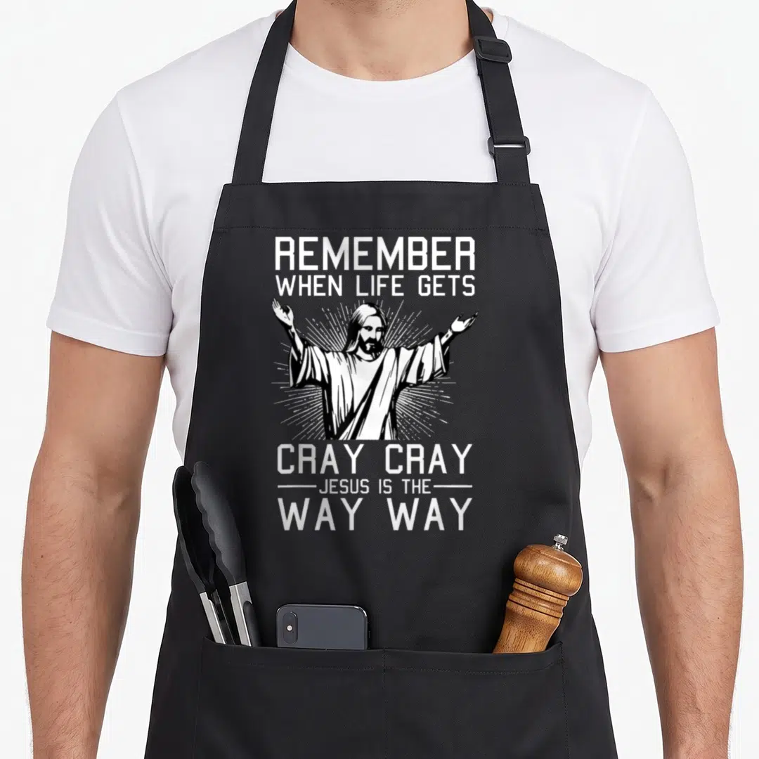 Way christmas apron - White line art of Jesus with arms raised surrounded by text about life getting cray cray — shown on a black cotton canvas apron against a white background