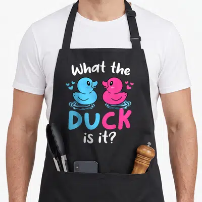 Zur h apron - Two cartoon ducks in blue and pink with text What the DUCK is it — shown on a black cotton canvas apron against a white background