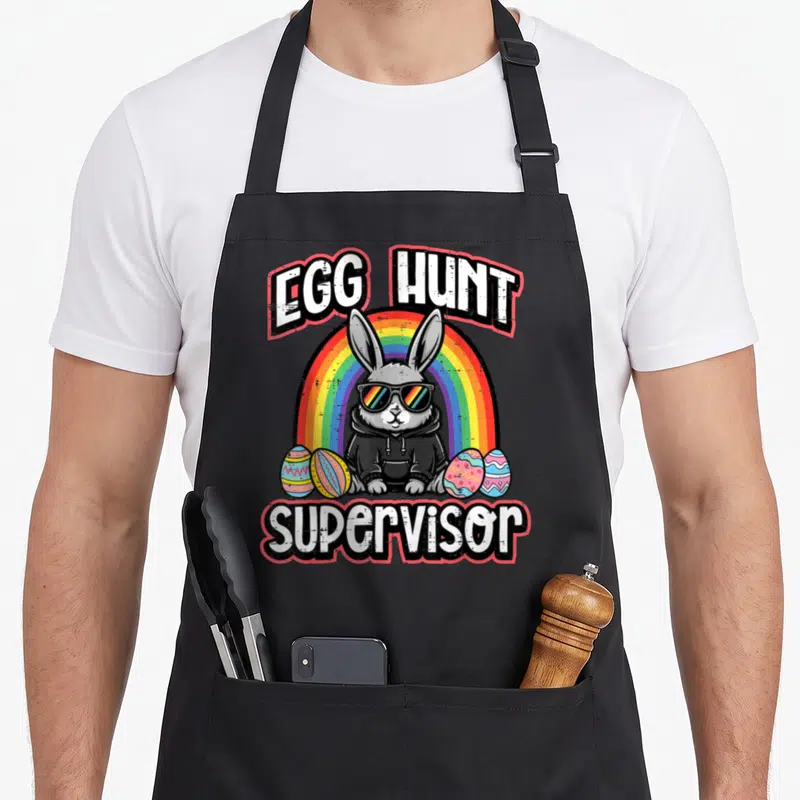 Hunt easter bunny aprons - Cartoon rabbit sunglasses rainbow four eggs EGG HUNT supervisor text — shown on a black cotton canvas apron against a white background