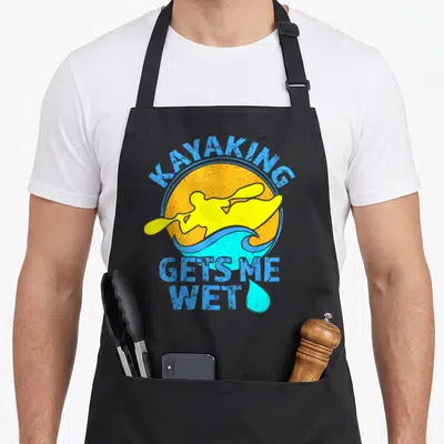 Kayak wet aprons - Retro yellow kayaker on blue wave with orange sun and stacked text — shown on a black cotton canvas apron against a white background