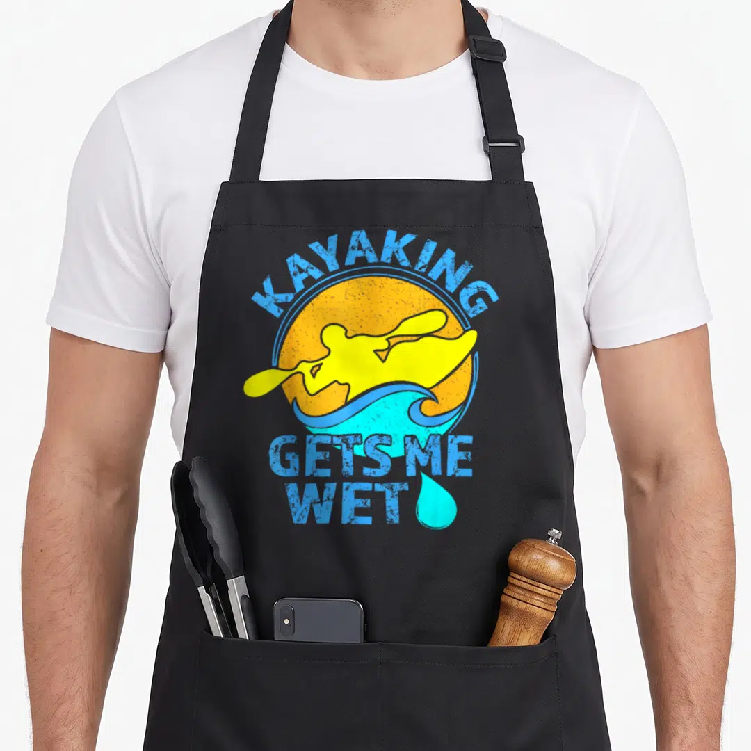Kayak wet aprons - Retro yellow kayaker on blue wave with orange sun and stacked text — shown on a black cotton canvas apron against a white background