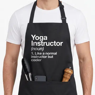 Definition grill instructor apron - White stacked text reading Yoga Instructor noun definition like normal but cooler — shown on a black cotton canvas apron against a white background
