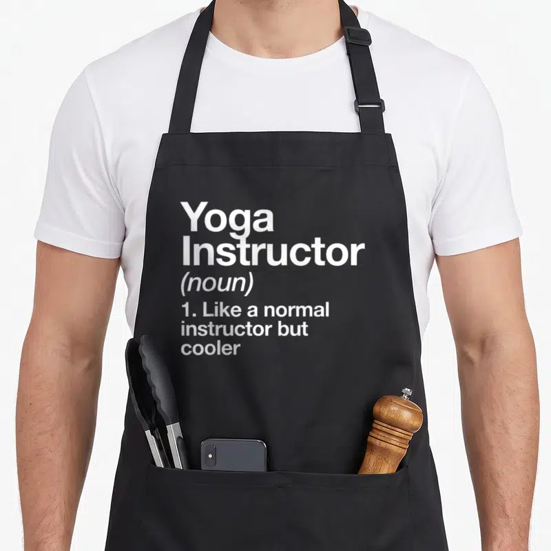 Definition grill instructor apron - White stacked text reading Yoga Instructor noun definition like normal but cooler — shown on a black cotton canvas apron against a white background