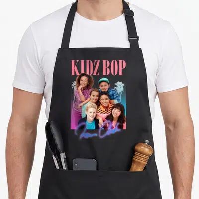 Kidz fan club apron - Photo of six children with KIDZ BOP text and palm trees in pink and blue — shown on a black cotton canvas apron against a white background