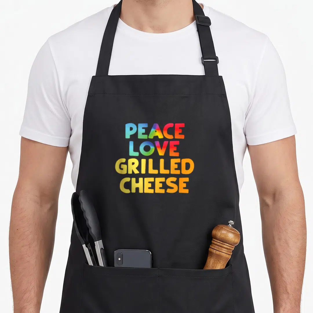Cheese grilled peaches apron - Stacked rainbow typography reading PEACE LOVE GRILLED CHEESE in bold letters — shown on a black cotton canvas apron against a white background