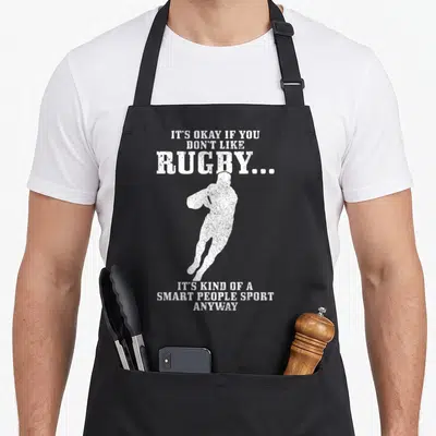 Rugby smart apron - White distressed rugby player silhouette surrounded by sarcastic text about the sport — shown on a black cotton canvas apron against a white background