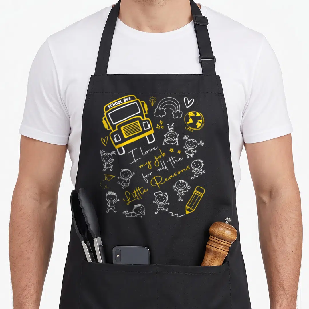 Reason bus driver apron - Yellow school bus doodle with I love my job text and scattered children drawings — shown on a black cotton canvas apron against a white background