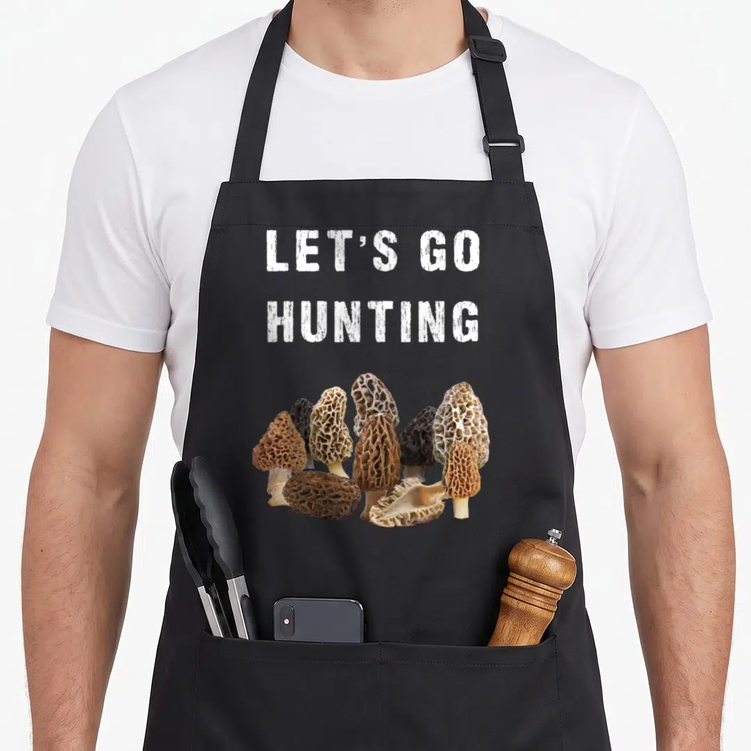 Outdoor foraging apron - LET'S GO HUNTING text above cluster of brown and tan morel mushrooms — shown on a black cotton canvas apron against a white background