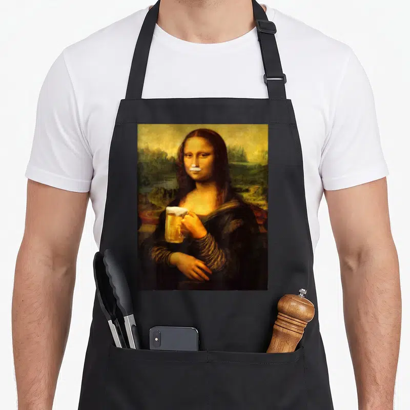 Mona beer apron - Mona Lisa holding beer mug with white foam mustache overlay in brown and gold tones — shown on a black cotton canvas apron against a white background