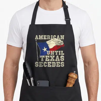 Texas cowboy apron - Distressed American until Texas secedes text over a waving white blue and red flag — shown on a black cotton canvas apron against a white background