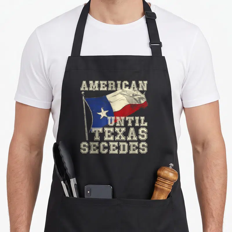 Texas cowboy apron - Distressed American until Texas secedes text over a waving white blue and red flag — shown on a black cotton canvas apron against a white background